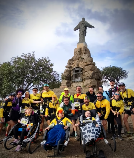 Equipo y niños en sillas de carreras adaptadas junto al Cristo de Sierra Blanca
